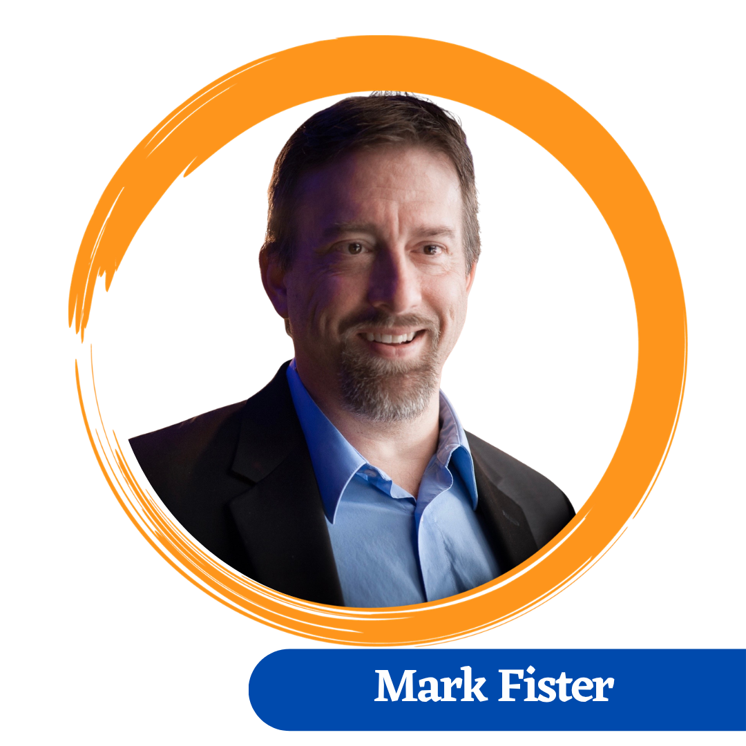 Mark has a goatee beard and is smiling. He is wearing a Dark jacket and a blue dress shirt